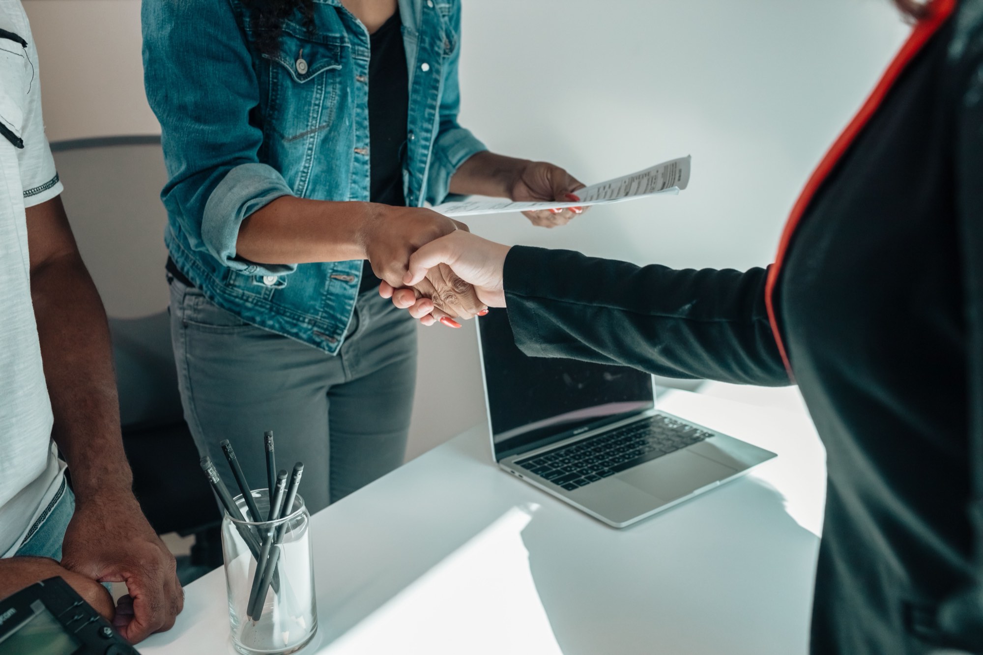 Two people shaking hands over a signed document at a desk